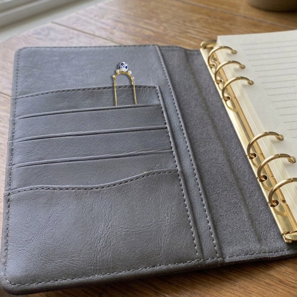A gray faux-leather ring binder wallet shown open, with card slots on the left, a gold-tone ring clip holding a ring, and a lined notebook page visible on the right. The wallet is photographed on a wooden tabletop.