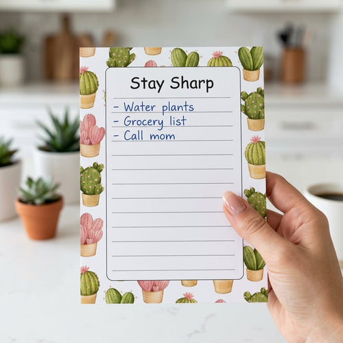 A hand holds a printed notepad with a cactus pattern border and the title 'Stay Sharp' on a white lined page, with a blurred kitchen background.