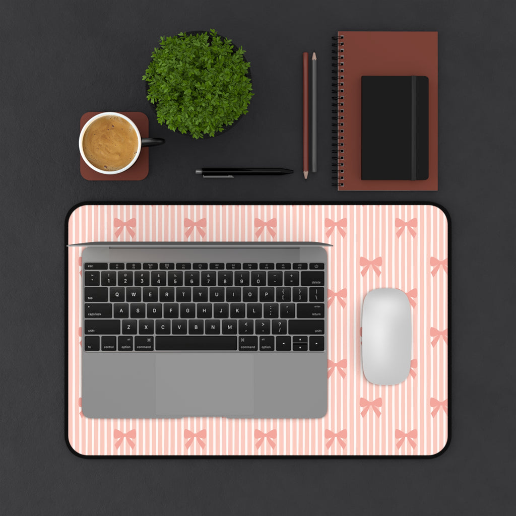 Laptop on a pink marble desk mat with a cup, plant, and stationery items on a black background.